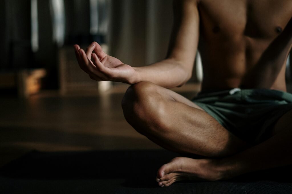 A shirtless man in a yoga studio meditating in the lotus position for relaxation and wellness.