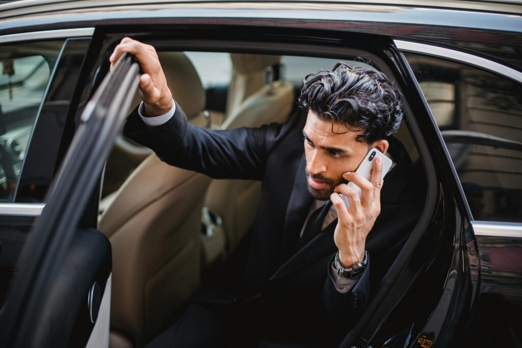 Professional man in a suit exits a luxury vehicle during a phone call, emphasizing a busy lifestyle.