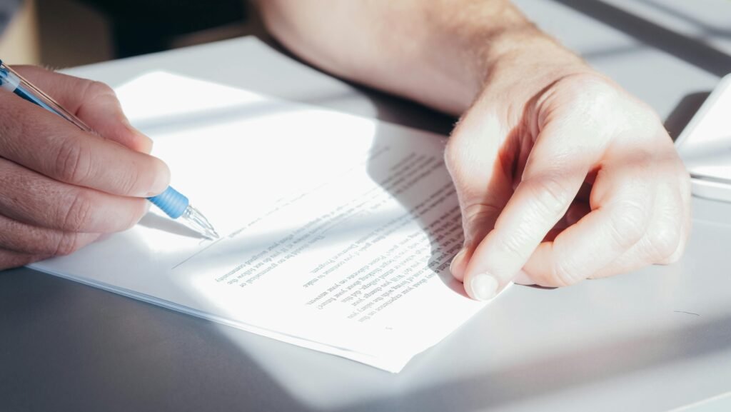 Hands signing a contract with a blue pen, close-up view.